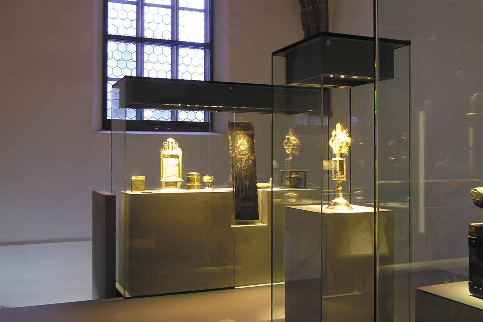 Das Referenzbild für Ausstellungsgestaltung aus der Dauerausstellung „Die Heiltumskammer“ zeigt eine Exponatpräsentation in einem Glaskubus mit Betonsockel.