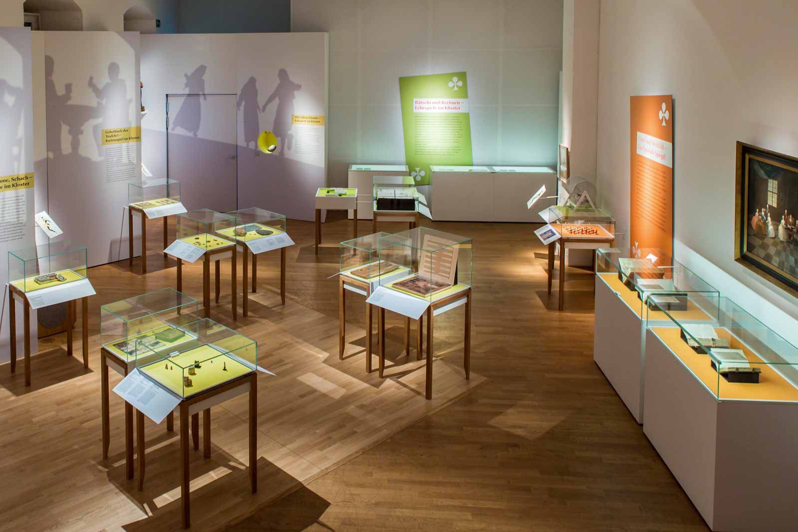Das Referenzbild für Ausstellungsgestaltung aus der Sonderausstellung „Heiter bis göttlich. Die Kultur des Spiels im Kloster“ zeigt eine Exponatpräsentation mit Tischvitrinen.