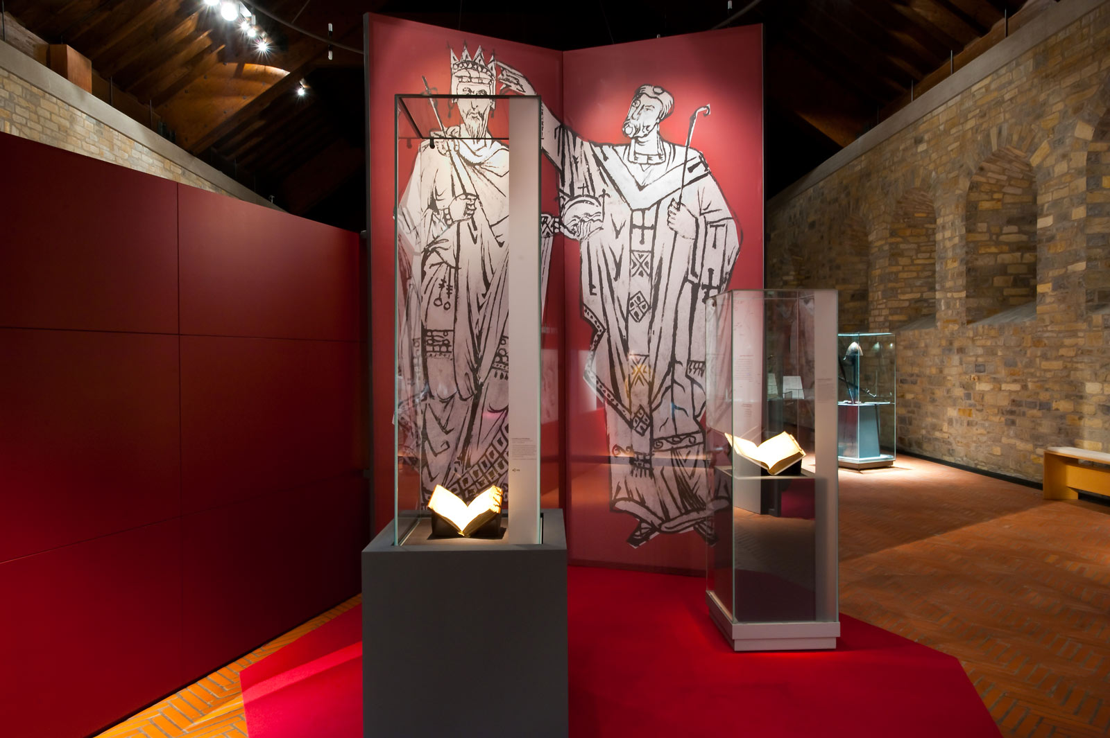 Das Referenzbild für Ausstellungsgestaltung aus der Sonderausstellung „Für Königtum und Himmelreich“ zeigt eine Szenografie mit Exponatpräsentation in Vitrinen.