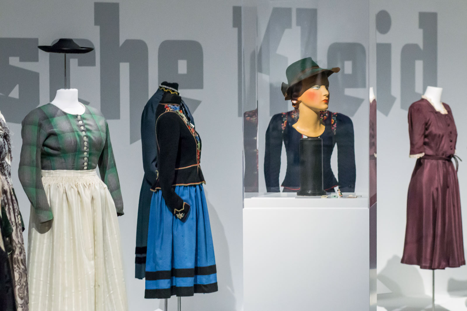 Das Referenzbild für Ausstellungsgestaltung aus der Sonderausstellung „Glanz und Grauen. Mode im Dritten Reich“ zeigt historische Kleidungsstücke in Ganzglasvitrinen und Vitrinen.
